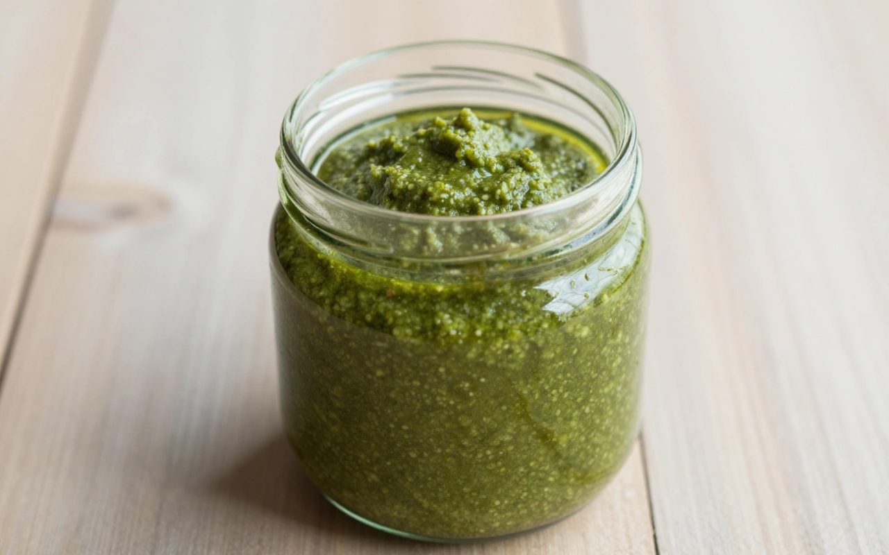 Vaso di vetro di pesto al basilico generico su un tavolo di legno con luce naturale.